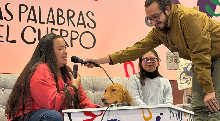 Una joven leyendo, al lado de su perro guía, y dos personas más, durante Tres personas en la tarima del salón B de Corferias durante el evento ‘Un horizonte que se expande: homenaje a 24 escritores con discapacidad de la literatura universal’.