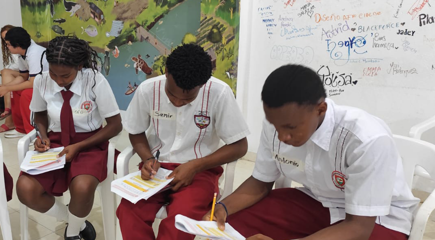 GeneraciónR31 Tres jóvenes con uniforme de colegio sentados escribiendo, durante un taller de Resiliencia y Compasión.