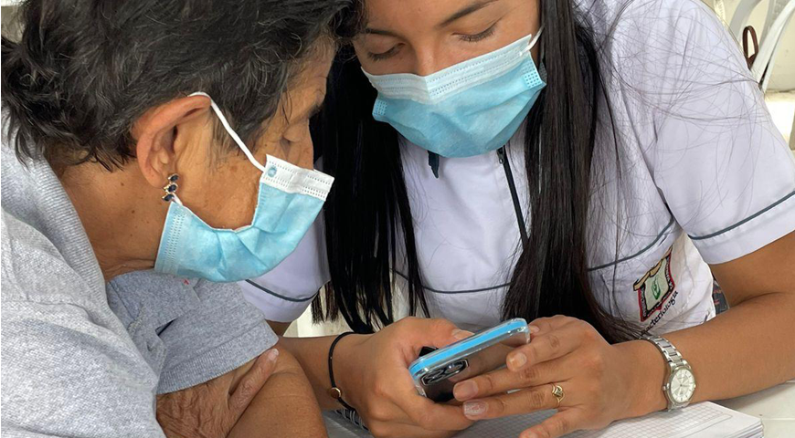 Una persona joven comparte un momento con una mujer mayor mientras revisan juntas el celular