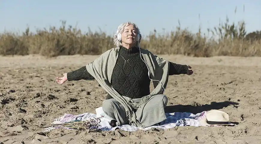 Mujer mayor sola, serena y feliz sentada en la arena, respirando plenamente, tranquila
