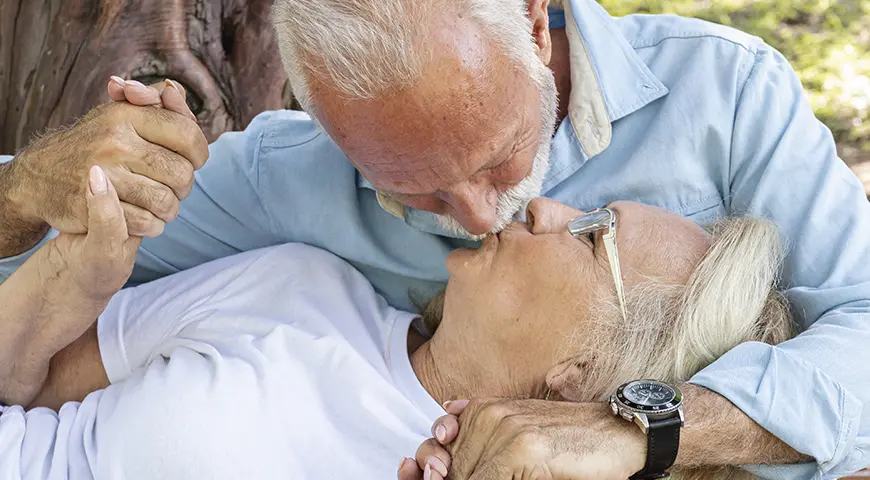 Un hombre y una mujer mayor se besan y toman de las manos con cariño